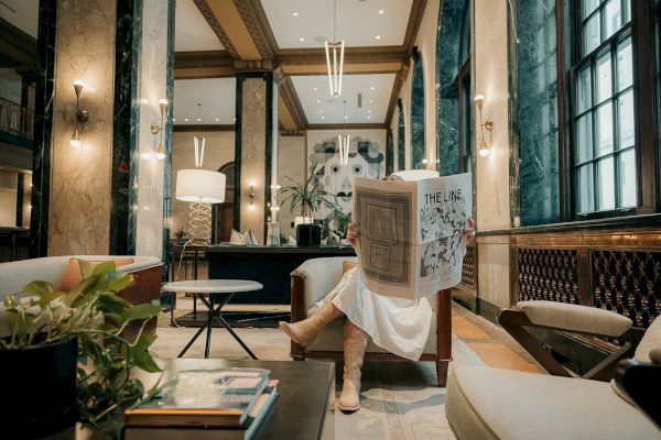 A person reads a newspaper in an elegant lounge with marble walls and modern decor.