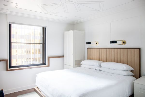 A modern bedroom with a bed, padded headboard, two wall-mounted lights, a window, and a white cabinet in a minimalist style.