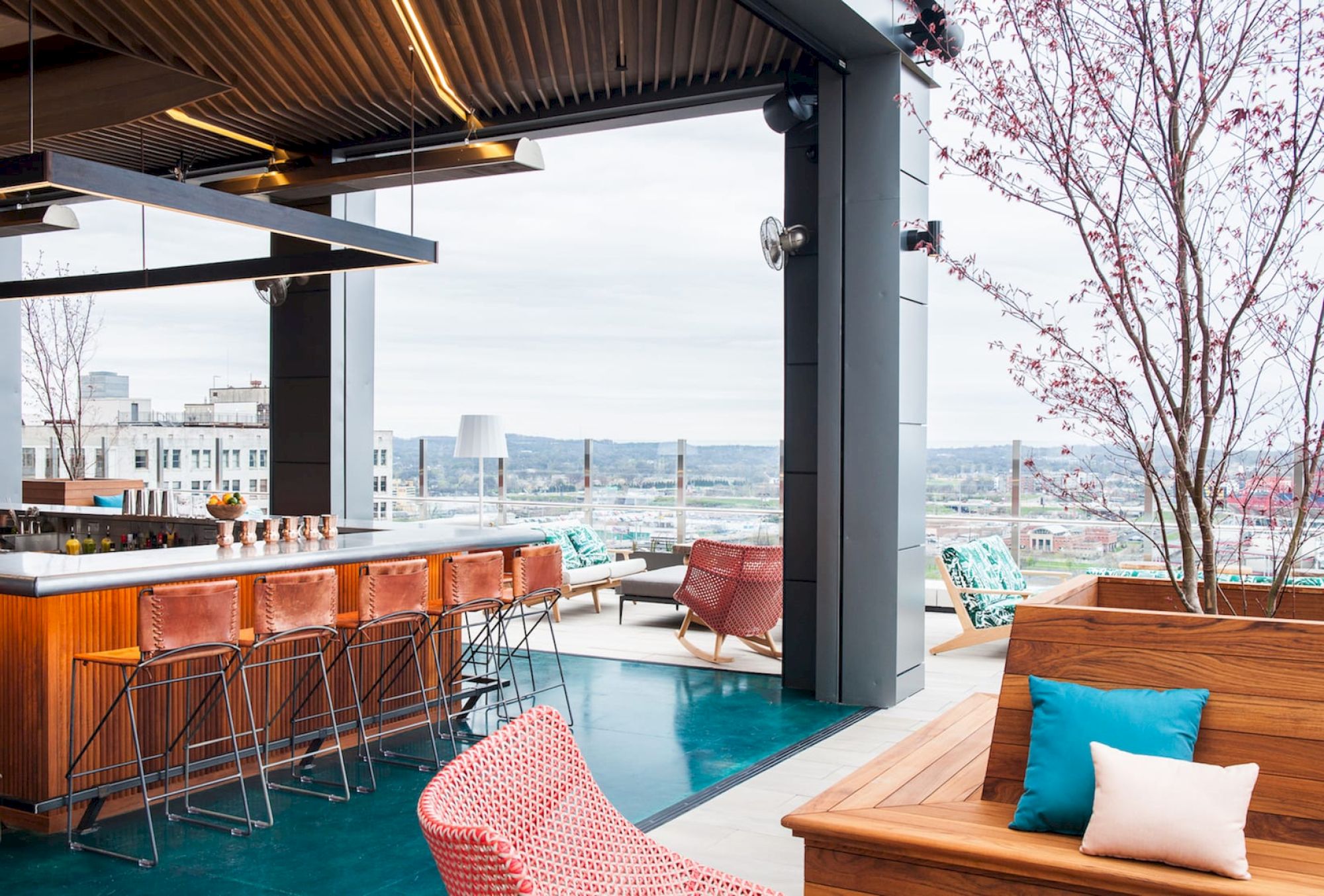 Rooftop lounge with modern decor, bar stools, cushioned seating, and a scenic city view. Open-air design with a relaxed atmosphere.