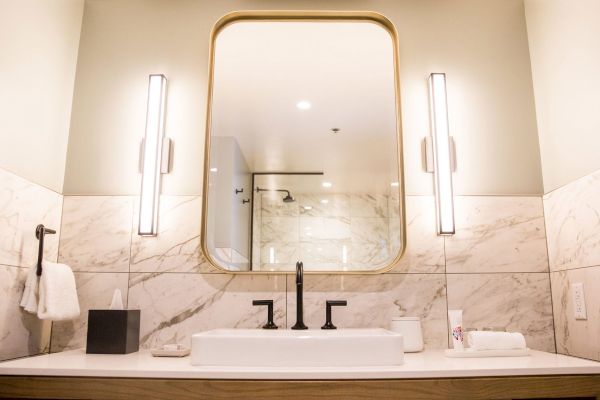 A modern bathroom with a large mirror, two vertical lights, a marble backsplash, and a counter with a sink and towels.