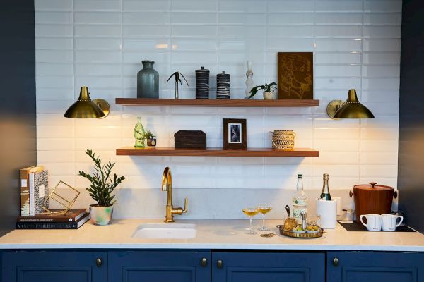 A modern kitchen counter with blue cabinets, open shelves, decorative items, and a sink, all set against white tile walls.