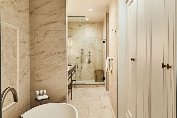 The image shows a modern bathroom with a bathtub, a glass-enclosed shower, beige tiles, and a vanity with a countertop.