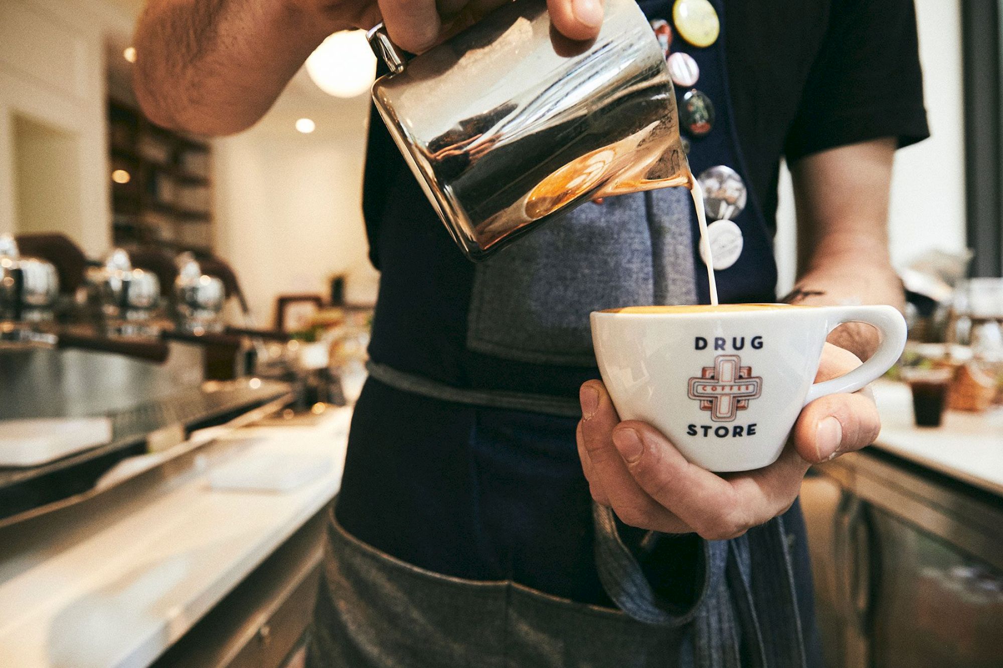 A person is pouring milk or cream into a coffee cup in a cafe setting.