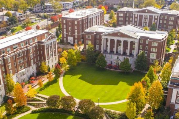 Aerial view of a campus with multiple brick buildings, green lawns, and trees, suggesting a university or college setting.