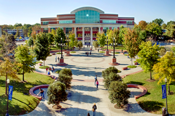 A college campus scene with buildings, a circular plaza, trees, and people walking around on a clear day.