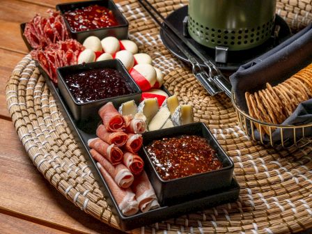 The image shows a charcuterie board with meats, cheeses, jams, and crackers arranged on a woven tray.