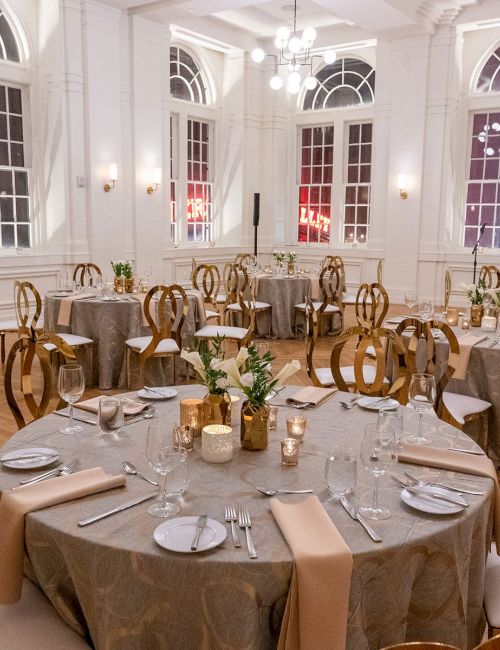 Elegant banquet hall with round tables set for an event, featuring floral centerpieces and soft lighting, creating a refined atmosphere.