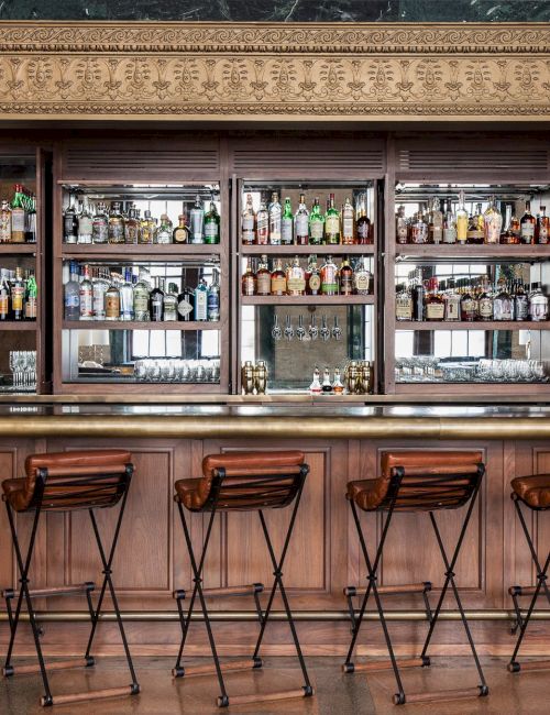 The image shows a classy bar with high chairs, a counter, and shelves stocked with various bottles of alcohol.