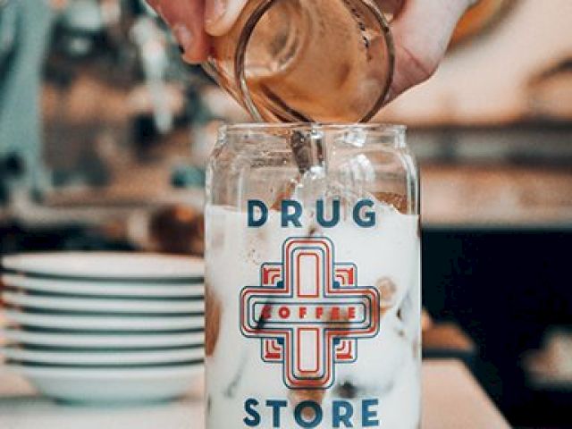 A hand pouring espresso into a jar with iced milk, labeled 