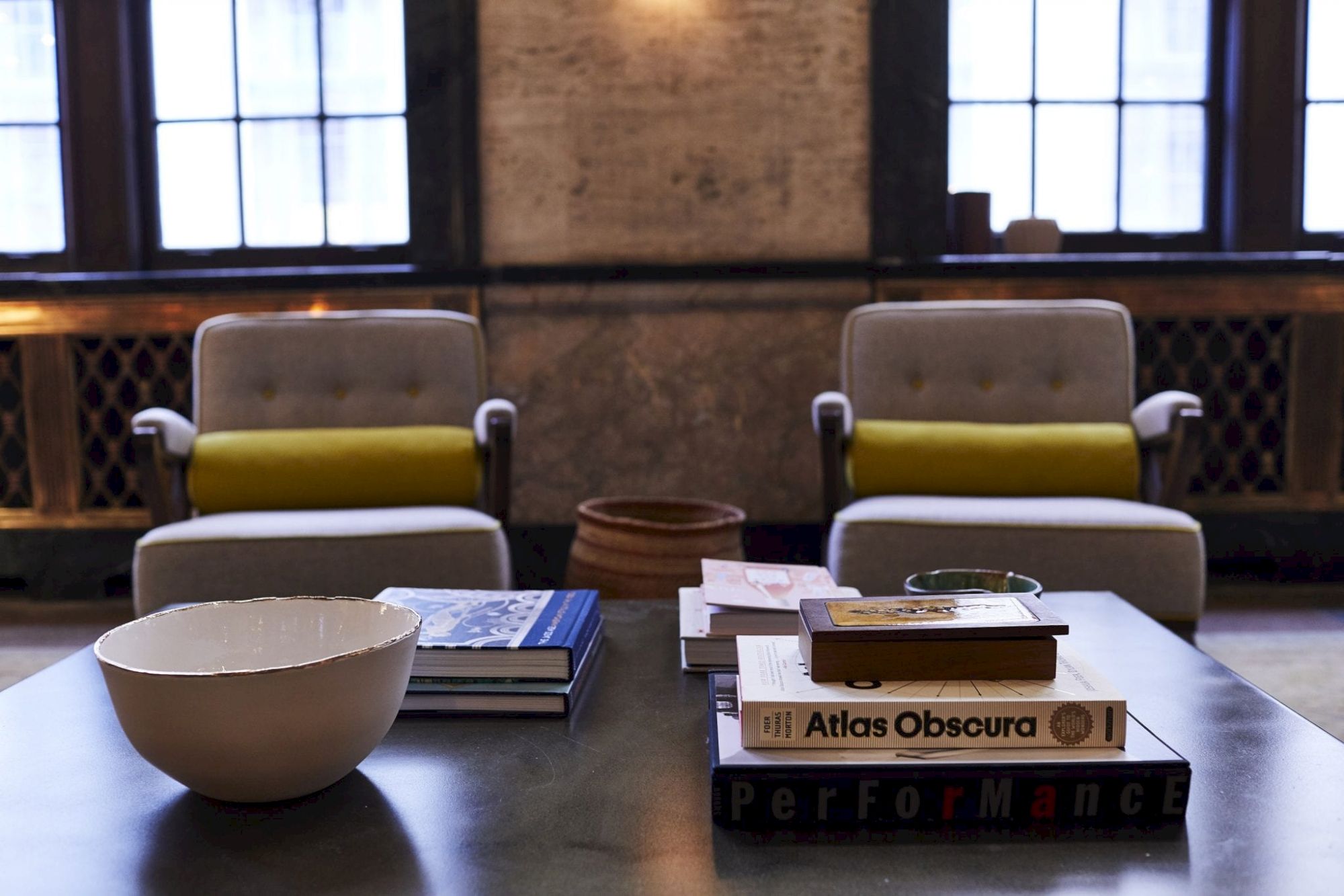 A cozy room with armchairs, books, and a bowl on a table. Books include 