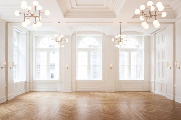 A bright, elegant room with large arched windows, hardwood floors, white walls, and modern chandeliers.