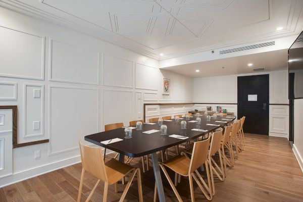 A modern conference room with a long table, surrounded by wooden chairs, set for a meeting with cups and napkins on the table.