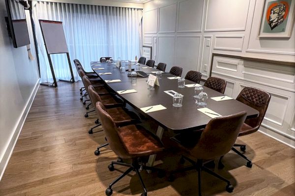 A conference room with a long table, chairs, notepads, glasses, a flip chart, and a wall-mounted TV, set in a modern, well-lit space.