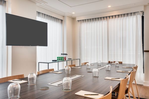 A conference room with a wooden table, chairs, notepads, a TV screen, and water glasses. Beverage bottles are on a side table.