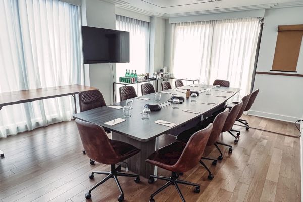 A conference room with a long table, chairs, a TV, notepads, and water bottles, set up for a meeting near large windows.