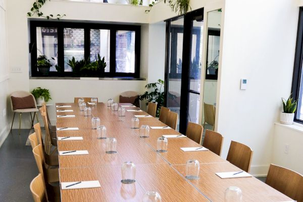 A modern conference room with a long wooden table, chairs, notepads, and glasses. Windows and plants create a fresh atmosphere.