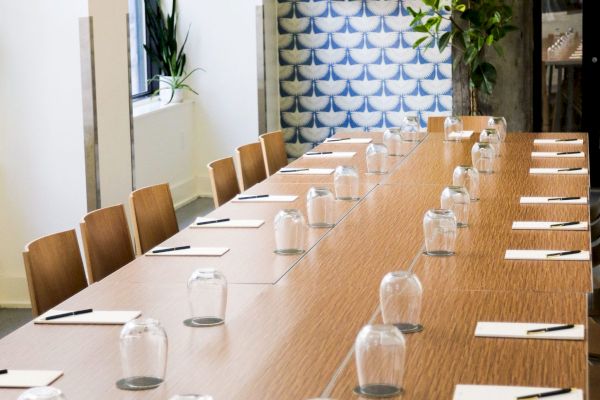 A conference room with a long table, glasses, notepads, and pens set out, surrounded by chairs and plant decorations.