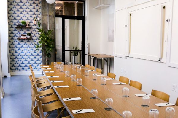 A modern conference room with a long table, chairs, notepads, and glasses. Decorative wall and plants enhance the bright atmosphere.