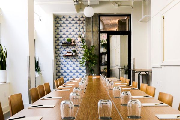 A long conference table set with notepads and glasses in a bright room, featuring patterned walls and plants, creates a modern meeting space.