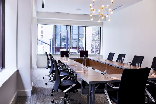 The image shows a modern conference room with a long table, black chairs, and large windows, illuminated by a stylish ceiling light.