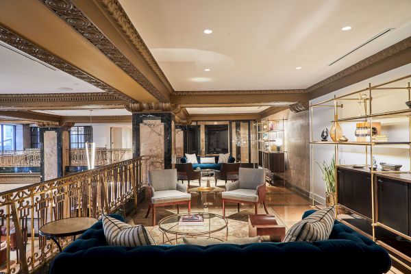 The image shows an elegantly decorated lounge area with plush seating, ornate ceilings, and modern shelves, creating a sophisticated ambiance.