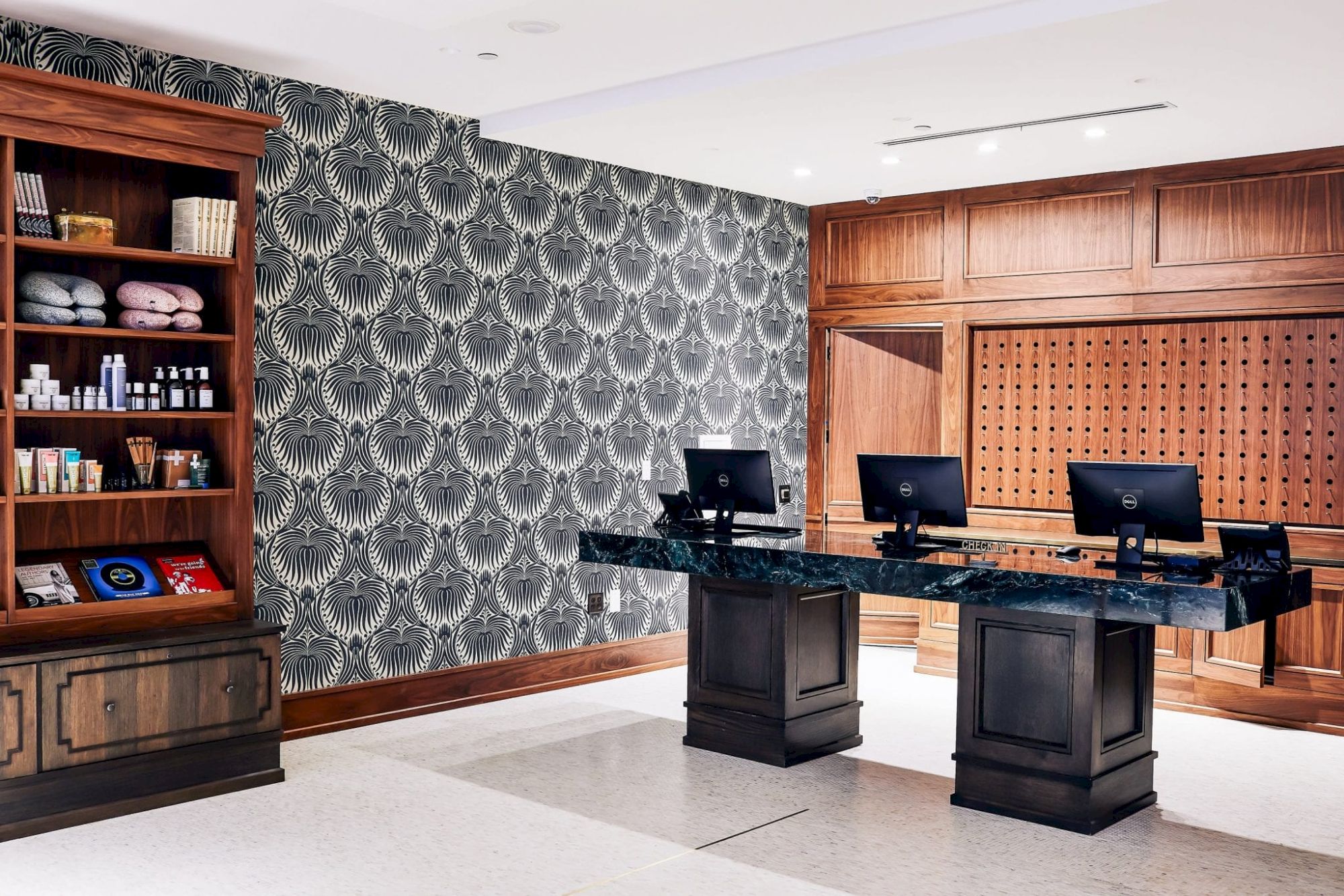 The image shows a reception area with two desks and computers, a patterned wall, and shelves with various items on the left side of the room.