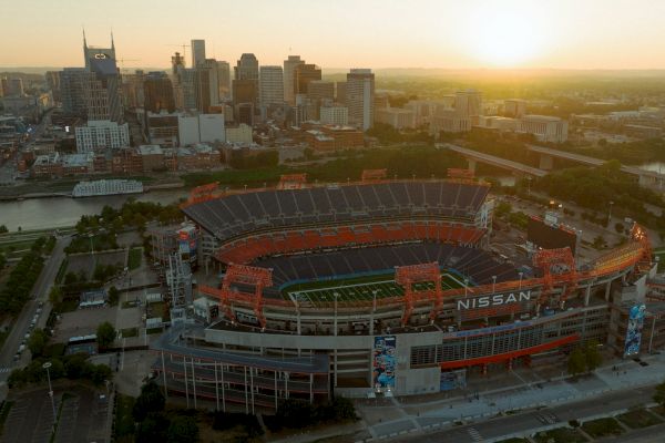 An aerial view of Nissan Stadium with a city skyline and a sunset in the background.