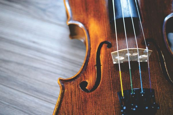 A close-up of a violin showing its strings and f-holes, placed on a wooden surface.