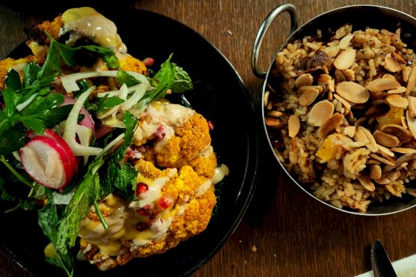 The image shows a dish with roasted cauliflower topped with greens and radishes, next to a bowl of rice garnished with sliced almonds.