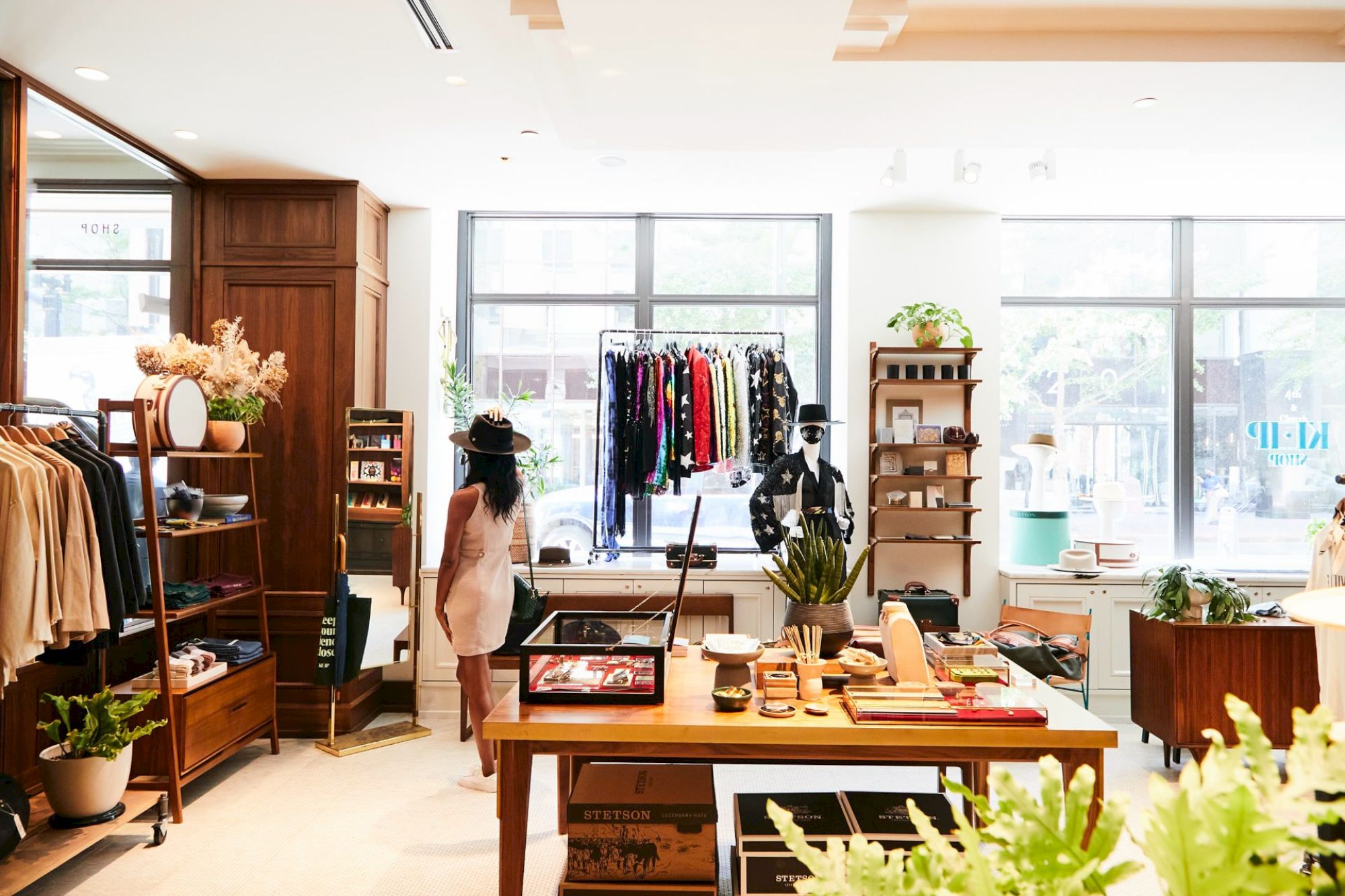 A boutique interior with clothing racks, shelves with accessories, and a person browsing. Bright and well-organized with natural light.