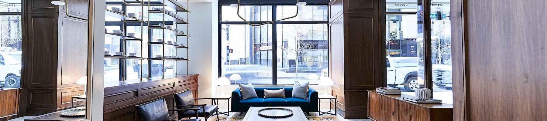 A modern, stylish living room with wooden furniture, blue sofa, large window, and decorative elements on the shelves.