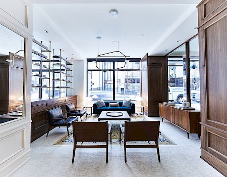 A modern living room with elegant wooden paneling, shelving, seating, a rug, and large windows allowing natural light to fill the space.