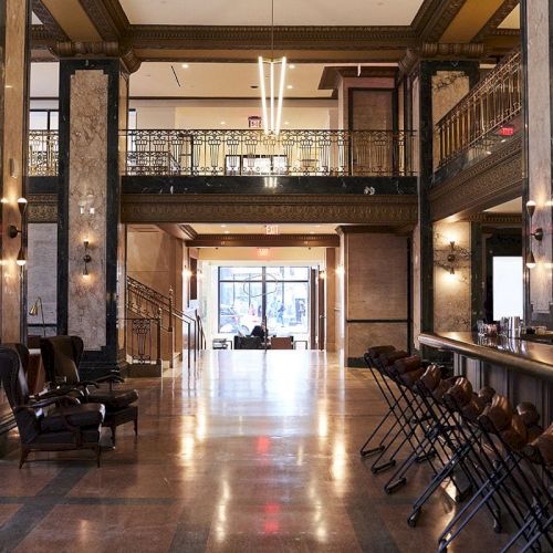 A spacious, elegant lobby with high ceilings, modern lighting, bar seating, and a view of the entrance in the background.