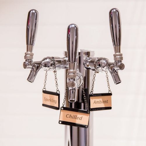 The image shows a set of three beverage taps labeled for sparkling, chilled, and ambient options, typically for dispensing different water types.