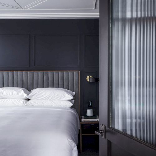 A modern bedroom with a neatly made bed, dark walls, and a frosted glass door is visible in the image.