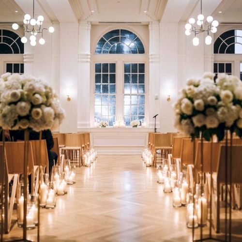 The image shows a beautifully decorated venue with white flowers and candles along the aisle, likely set up for a wedding ceremony.