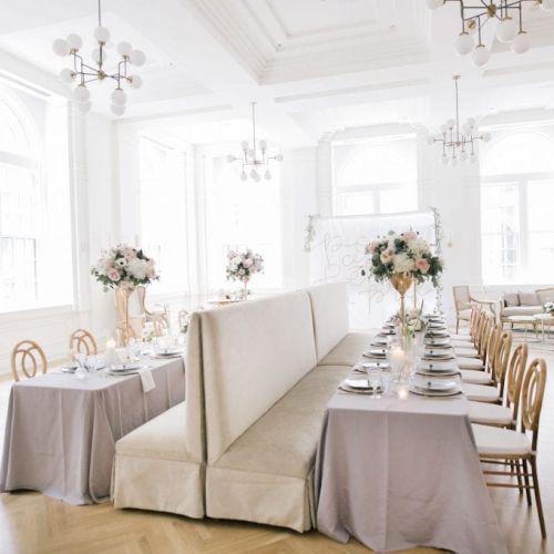 The image shows an elegantly decorated dining room with long tables, floral centerpieces, and a light, airy atmosphere.