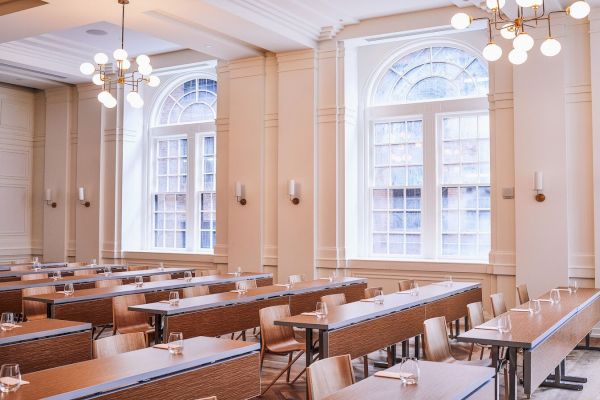 The image shows an empty conference room with long tables, chairs, large windows, and chandeliers, designed with a neutral color palette.