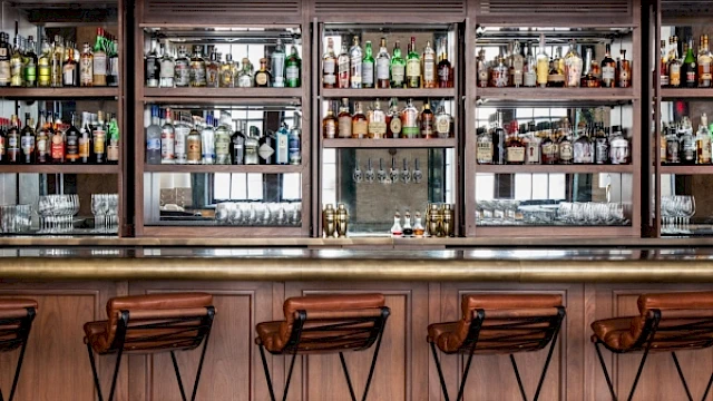 A well-stocked bar with wooden stools lined up in front of shelves filled with various bottles and glasses, creating a cozy atmosphere.