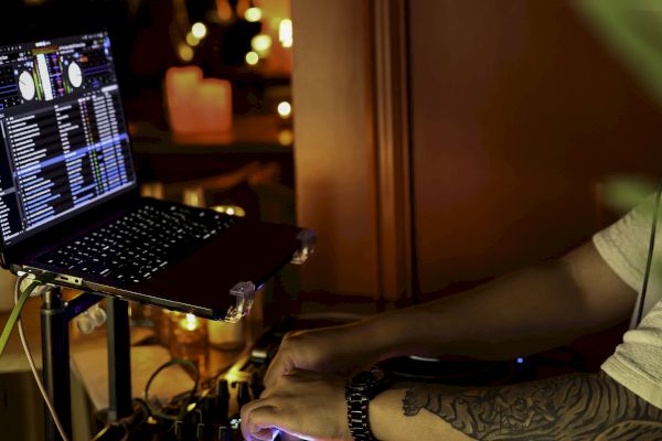 A DJ is mixing tracks on a turntable with a laptop in a dimly lit setting, creating a vibrant ambiance with atmospheric lighting.