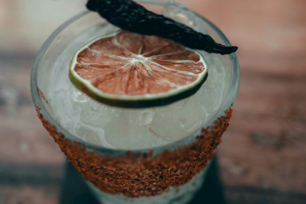 A cocktail in a glass with a salted rim, garnished with a dried lime slice and a chili pepper on top.