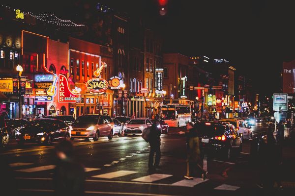 A lively street scene at night featuring neon signs, bustling people, and traffic, evoking a vibrant urban nightlife atmosphere.