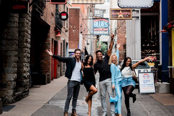 A lively group posing in a vibrant alleyway with colorful signs for various venues like a theatre and pub.