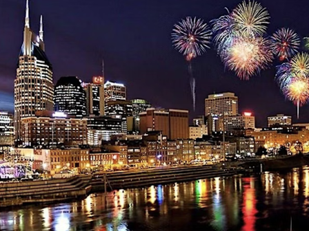 City skyline at night with fireworks illuminating the sky, reflecting on a river.