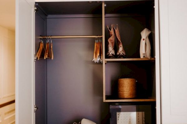 An open wardrobe with hangers, a safe, shelves with some items, and a bag.