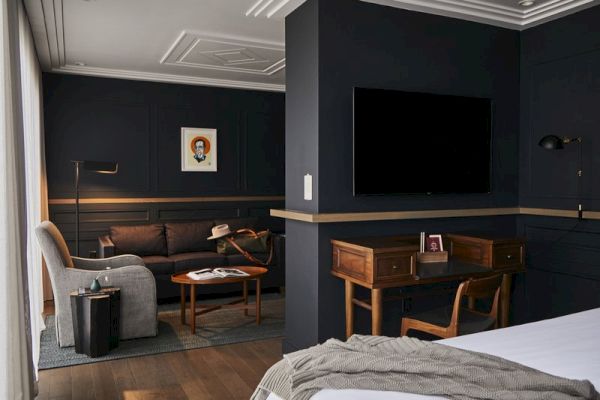 A modern living space with dark walls, a TV, a sofa, a desk, an armchair, and decor accents, creating a cozy, sophisticated atmosphere.