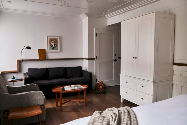 The image shows a cozy room with a black sofa, wooden coffee table, armchair, wardrobe, and artwork on the wall, exuding a modern vibe.