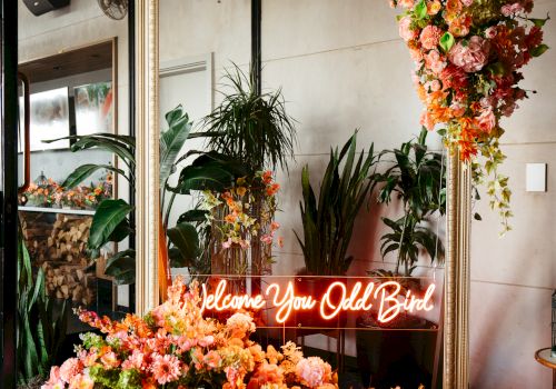 A large mirror adorned with vibrant flowers, a neon sign reading 