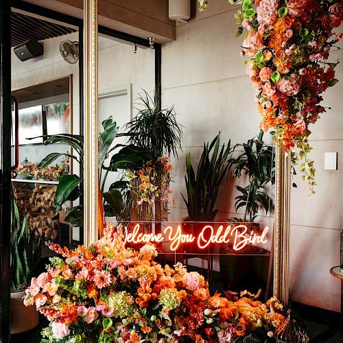 A large mirror adorned with vibrant flowers, a neon sign reading 