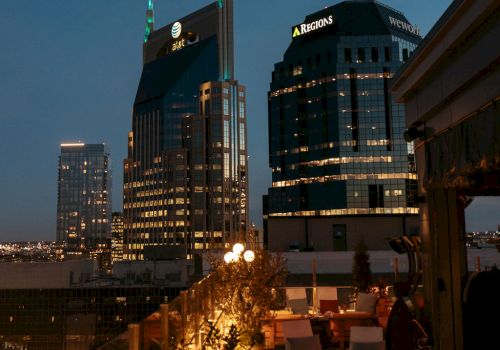 Rooftop view of a cityscape at dusk with illuminated buildings and cozy seating on the terrace for relaxation.